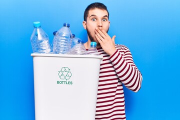Young handsome man recycling plastic bottles covering mouth with hand, shocked and afraid for...