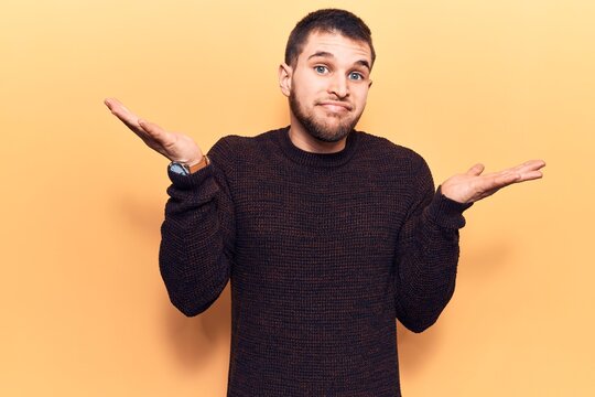 Young handsome man wearing casual sweater clueless and confused with open arms, no idea and doubtful face.