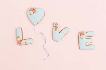 Gingerbread heart, cookies in shape of letter love with icing on pastel pink background. Valentines day composition or greeting postcard with copy space for text. Minimal style.