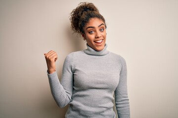 Beautiful african american girl wearing turtleneck sweater standing over white background smiling with happy face looking and pointing to the side with thumb up.