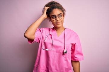 African american nurse girl wearing medical uniform and stethoscope over pink background confuse and wonder about question. Uncertain with doubt, thinking with hand on head. Pensive concept.