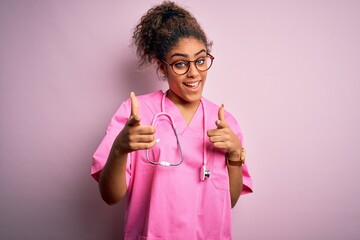 African american nurse girl wearing medical uniform and stethoscope over pink background pointing fingers to camera with happy and funny face. Good energy and vibes.
