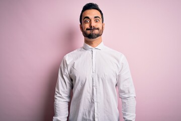 Young handsome man with beard wearing casual shirt standing over pink background puffing cheeks with funny face. Mouth inflated with air, crazy expression.