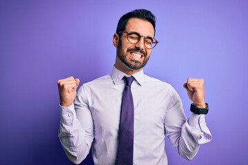 Handsome businessman with beard wearing casual tie and glasses over purple background very happy and excited doing winner gesture with arms raised, smiling and screaming for success. Celebration