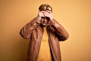 Fototapeta na wymiar Young handsome redhead man wearing casual leather jacket over isolated yellow background suffering from headache desperate and stressed because pain and migraine. Hands on head.
