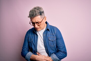 Young handsome modern man wearing glasses and denim jacket over pink isolated background with hand on stomach because nausea, painful disease feeling unwell. Ache concept.