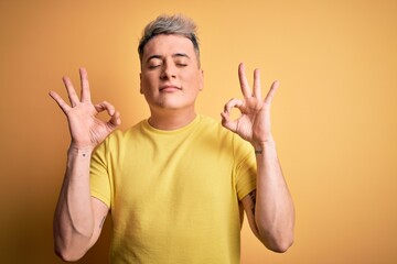 Naklejka premium Young handsome modern man wearing yellow shirt over yellow isolated background relaxed and smiling with eyes closed doing meditation gesture with fingers. Yoga concept.