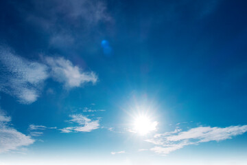 Beautiful sunny clear blue sky background with sun light rays & spectrum flares shining through soft white cirrocumulus clouds or cirrostratus cloudscape on bright daylight horizon in tropical summer 