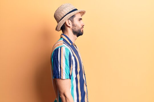 Young handsome man with beard wearing summer hat and shirt looking to side, relax profile pose with natural face with confident smile.