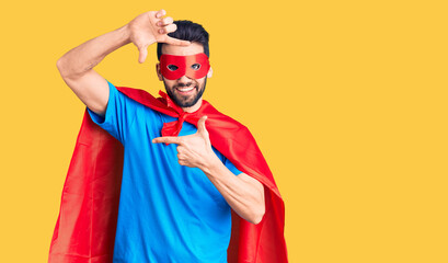 Young handsome man with beard wearing super hero costume smiling making frame with hands and fingers with happy face. creativity and photography concept.