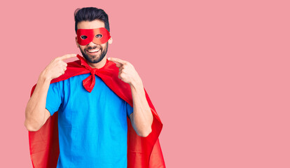 Young handsome man with beard wearing super hero costume smiling cheerful showing and pointing with fingers teeth and mouth. dental health concept.