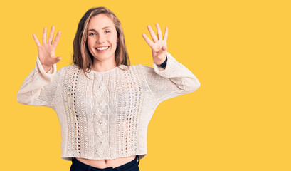 Young beautiful blonde woman wearing casual sweater showing and pointing up with fingers number...