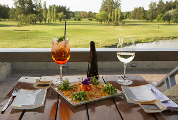 Gourmet food. Elegant sushi restaurant. Outside table set up and dish presentation. Raw salmon sushi plate with white wine and drink, with a beautiful golf course and lake view in the background. 