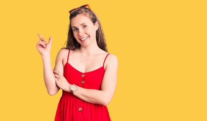 Young beautiful blonde woman wearing casual dress with a big smile on face, pointing with hand and finger to the side looking at the camera.