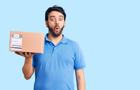 Young hispanic man holding delivery package scared and amazed with open mouth for surprise, disbelief face
