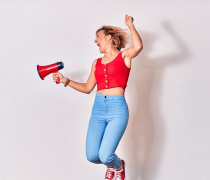 Young beautiful caucasian woman screaming using megaphone. Jumping over isolated white background
