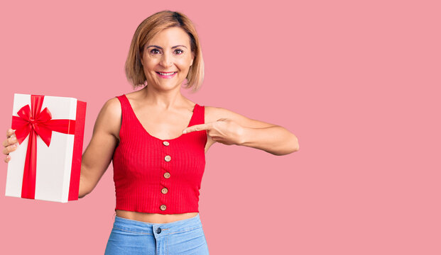 Young blonde woman holding gift pointing finger to one self smiling happy and proud