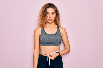 Young blonde sporty woman with blue eyes controlling weight using tape measure on waist with a...