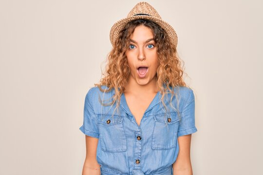 Young beautiful woman with blue eyes wearing casual denim dress and summer hat afraid and shocked with surprise expression, fear and excited face.