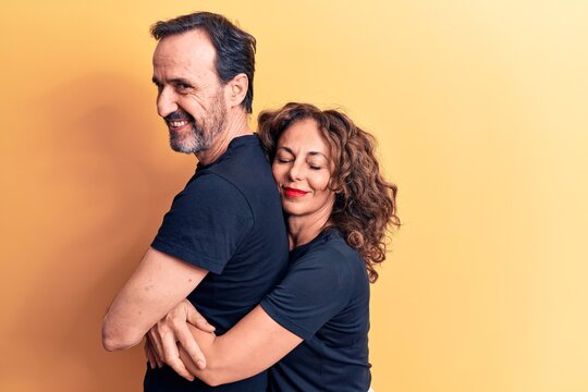 Middle age beautiful couple wearing t-shirt standing over isolated yellow background hugging oneself happy and positive, smiling confident. Self love and self care