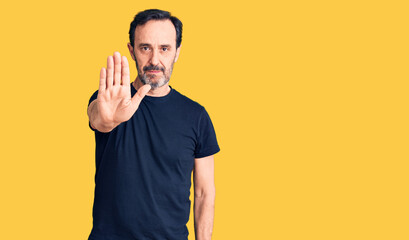 Middle age handsome man wearing casual t-shirt doing stop sing with palm of the hand. warning expression with negative and serious gesture on the face.