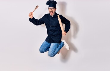 Middle age handsome hispanic man wearing glasses and cook uniform smiling happy. Jumping with smile...