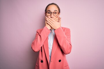 Young beautiful businesswoman wearing jacket and glasses over isolated pink background shocked covering mouth with hands for mistake. Secret concept.