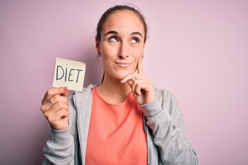 Young beautiful sporty woman doing sport holding reminder paper with diet message serious face...