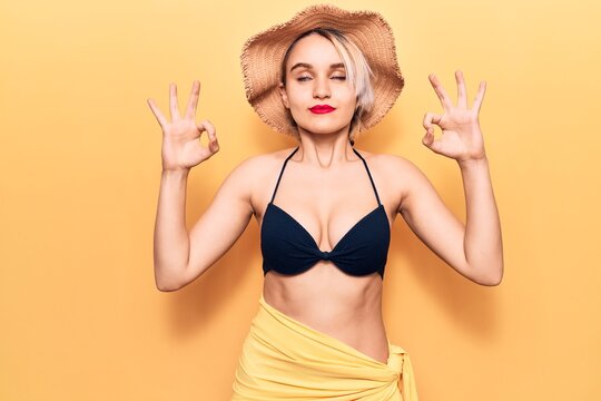 Young beautiful blonde woman wearing bikini and summer hat relax and smiling with eyes closed doing meditation gesture with fingers. yoga concept.