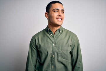 Young brazilian man wearing casual shirt standing over isolated white background looking away to side with smile on face, natural expression. Laughing confident.