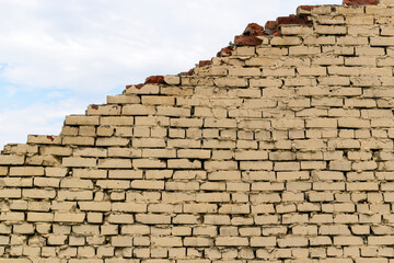 Ruined brick wall diagonally. Red brick with old paint. Color - Ecru, Hue Brown. Blue sky with clouds.