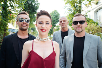 Beautiful smiling female singer with bright make-up and music band members standing outdoors