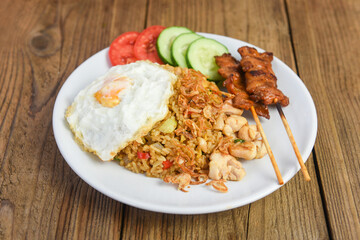 Nasi goreng fried rice chicken with egg tomato cucumber on white plate and satay with sauce - Nasi Goreng Ayam indonesian food Asian