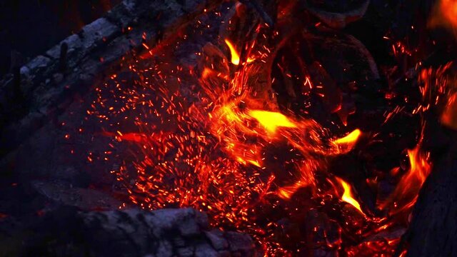 Slow motion of an open pit fire being stoked with a burning log.