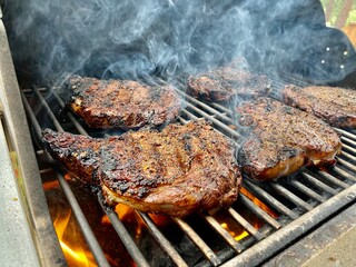 ribeye steaks are cooking on a grill with smoke coming up