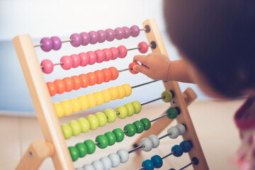 asian little adorable baby toddler girl using math montessori with colorful bead, playing and learning using hands moving each bead calculating on early age development on statistics skills concept