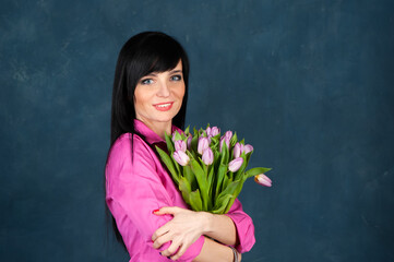 Trendy beautiful girl, brunette in a bright pink shirt, with a bouquet of tulips flowers, looking at the camera, the theme of summer, spring.