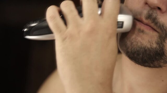 a man shaves his stubble. the guy cleans his beard with an electric razor. morning treatments in the bathroom. half of the beard close-up. copy space
