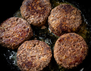 Beef burgers fried in frying pan.