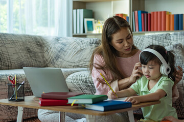 A Beautiful Asian mother busy working while looking after and teaching her children on a laptop computer at home