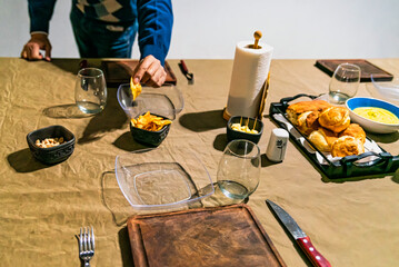 man holding french fries at a family home table prepared to celebrate the gathering of friends, with sauces, cheese, wine and dishes.