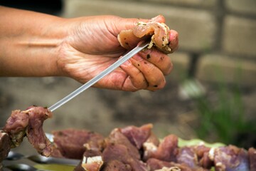 A hand puts kebab meat on a skewer
