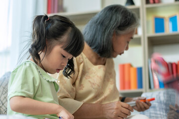 A kind and gentle Asia grandmother teaching her granddaughter to read write and drawing on a white board at home