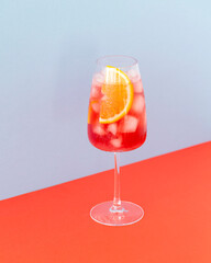 Aperol cocktail on a colors background. Cold drink with ice cubes. Glass of aperol spritz with orange. Summer Italian cocktail. Selective focus