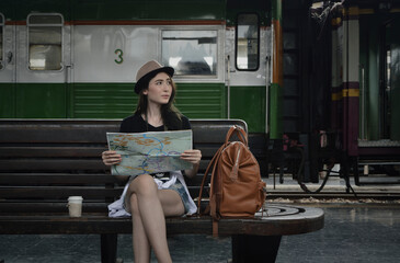 Fototapeta na wymiar Young beautiful woman traveler holding travel map sitting on wooden old chair with backpack and coffee cup in train station, Business travel holiday relaxation concept