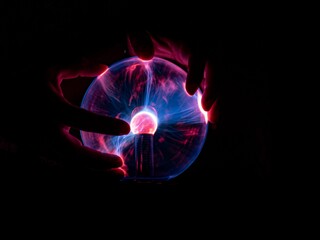 Isolated shot of hands on an illuminating plasma ball in front of a black background