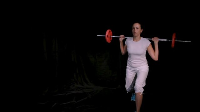 Woman performs lunges with barbell.Copy space.Isolated on black background.Long shot.Hot Iron.