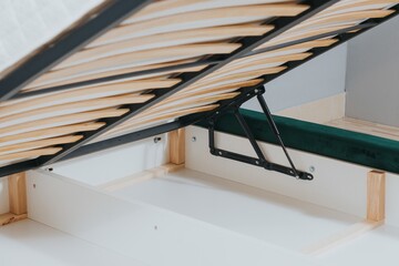 Closeup shot of a bed with wooden frame and lifting mechanism for a storage space