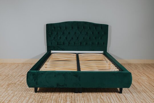 Bed With Green Fabric Upholstery And A Wooden Frame Without Mattress In An Empty Room