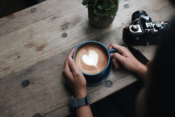 Close-up of a woman hand holding a latte coffee on a wooden table and film camera..